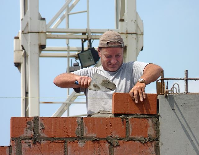 Een metselaar legt een steen met de troffel