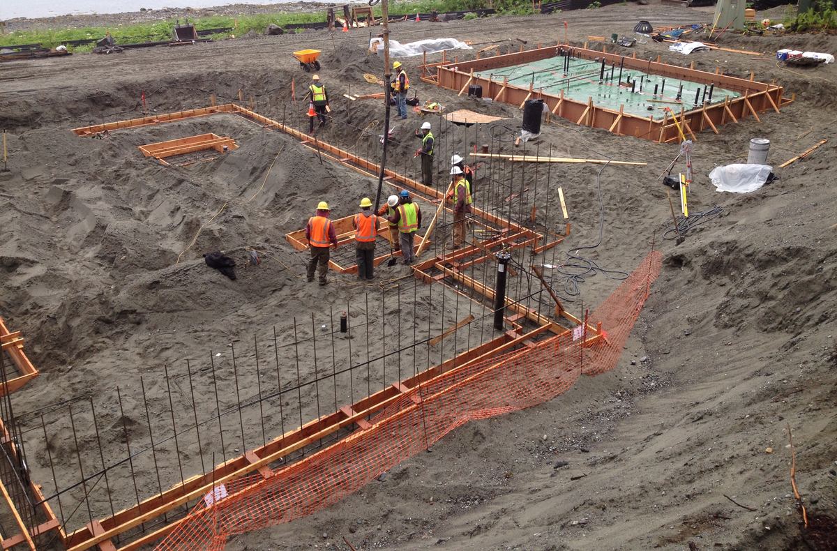 Een bouwput met bekisting en wapening voor de fundering; arbeiders in fluohesjes aan het werk